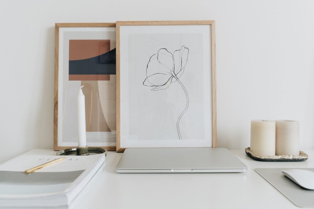 Elegant minimalist home office desk setup with framed art, candles, and a closed laptop.